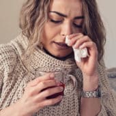 Woman with a cold, hot drink in hand and wiping her nose with a tissue